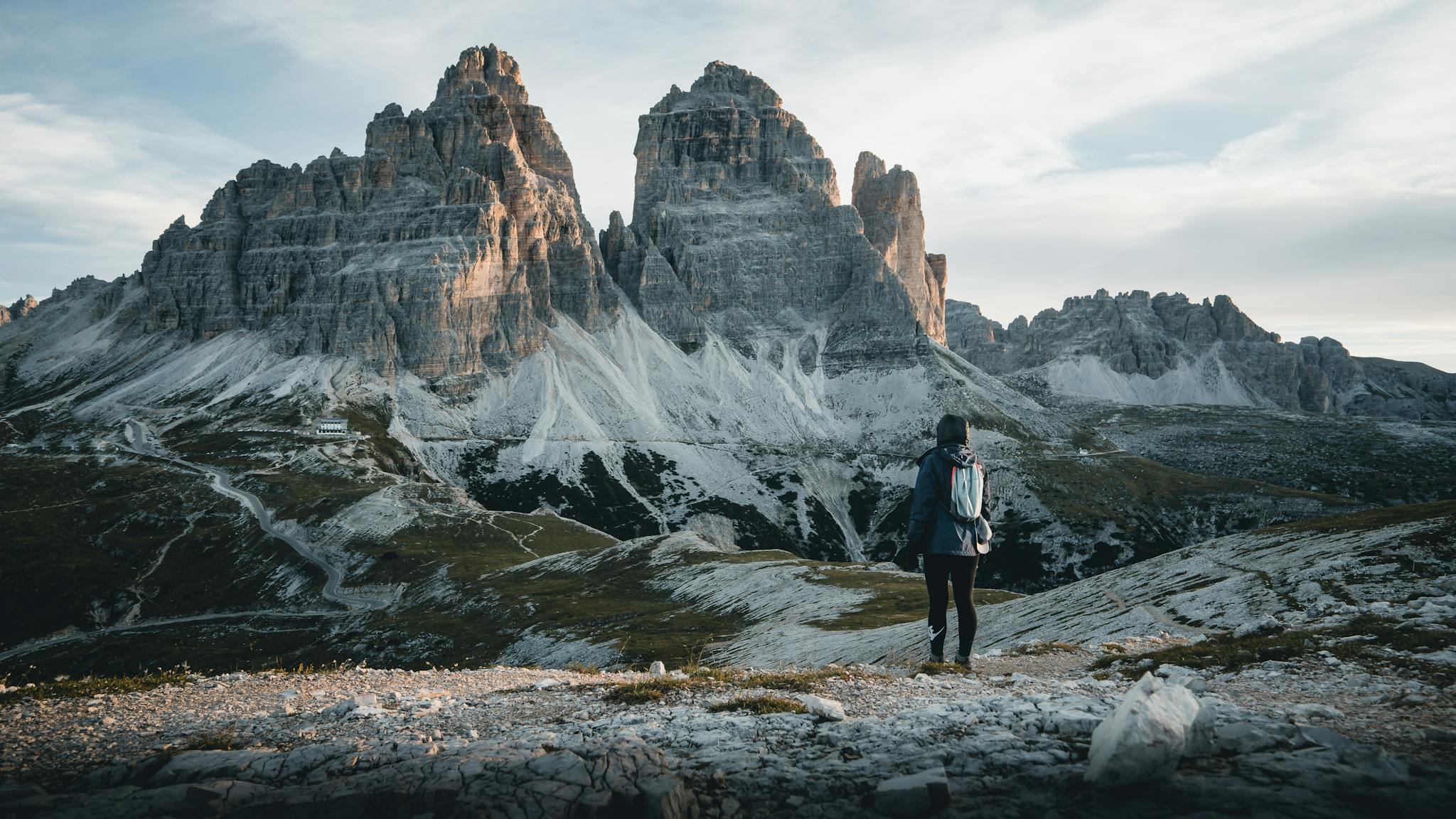 A hiker admires the majestic Tre Cime di Lavaredo in the Italian Dolomites, perfect for travel enthusiasts.