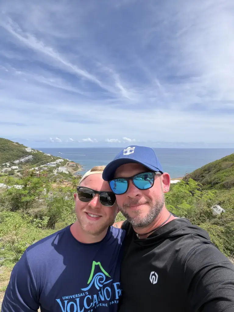 Fox and Brandon smiling at a hilltop overlook with blue water and green islands behind them
