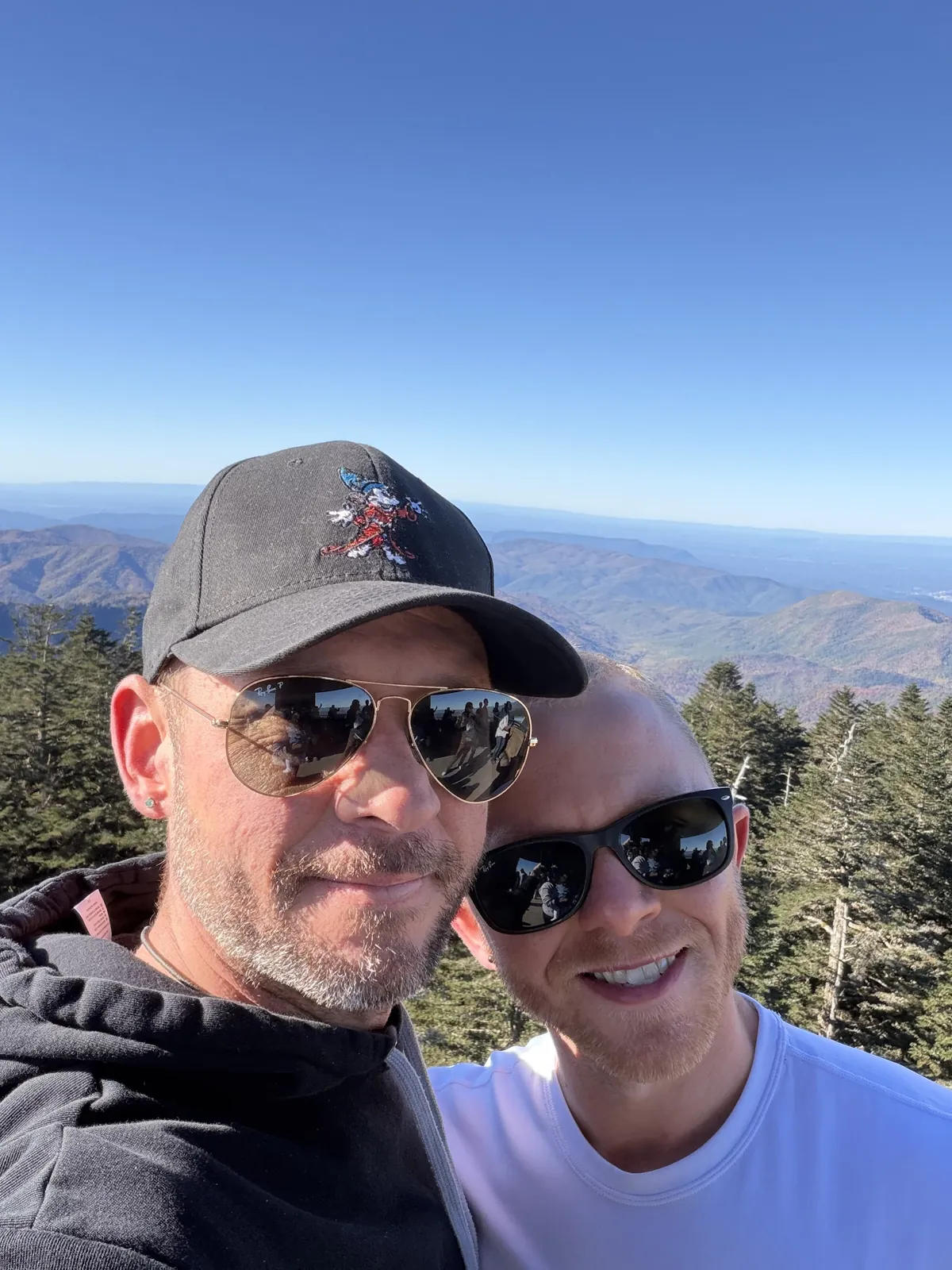 Fox and Brandon smiling in sunglasses with layered mountain ridges behind them