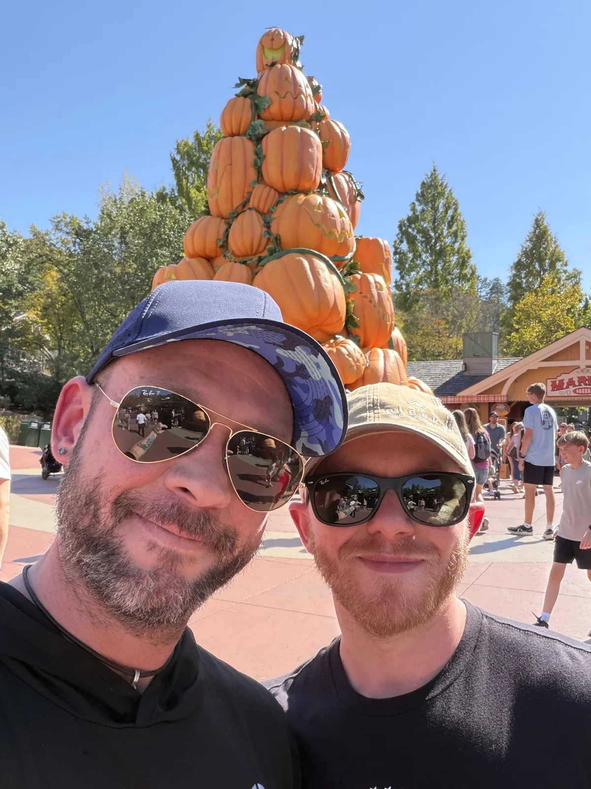 Fox and his husband taking a selfie in front of a tall tower of stacked pumpkins at Dollywood